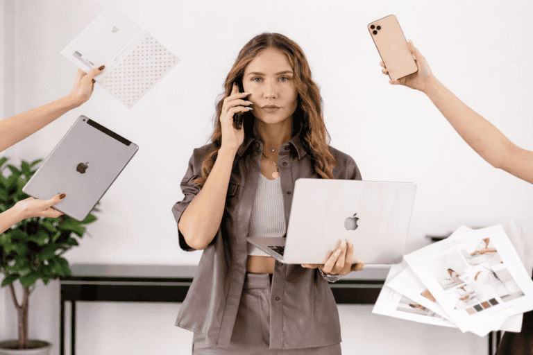 Eine Hochzeitsplanerin steht in einem hellen Arbeitsumfeld und jongliert Laptop, Smartphone und Unterlagen – Sinnbild für viele Anfragen ohne klaren Überblick.