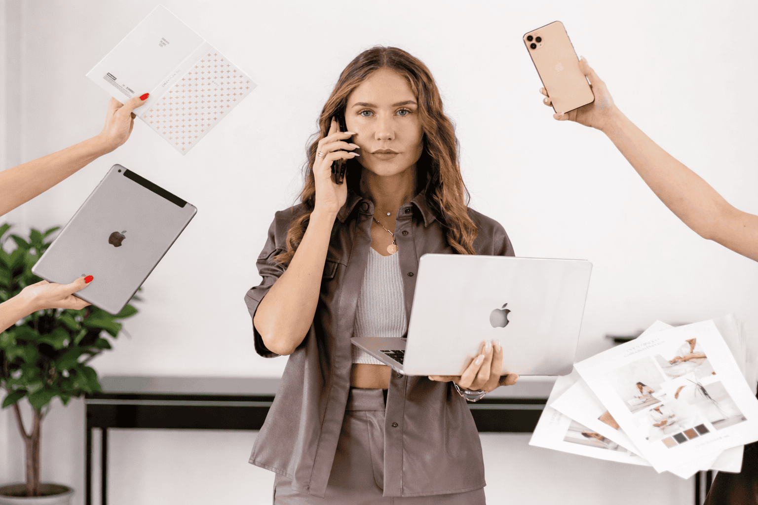 Eine Hochzeitsplanerin steht in einem hellen Arbeitsumfeld und jongliert Laptop, Smartphone und Unterlagen – Sinnbild für viele Anfragen ohne klaren Überblick.