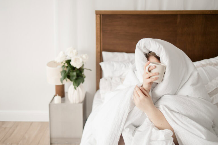 Erschöpfte Hochzeitsplanerin sitzt morgens im Bett mit einer Tasse Kaffee – Sinnbild für Überforderung und Ausbrennen in der Hochzeitsplanung.