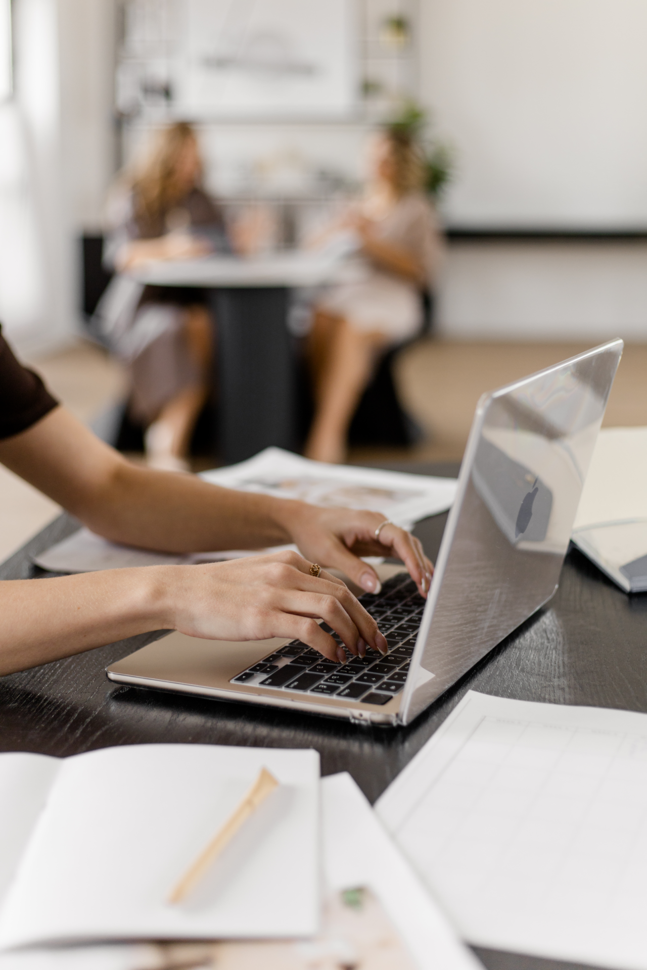 Soloselbständige arbeitet am Laptop, im Hintergrund findet ein Beratungsgespräch statt.